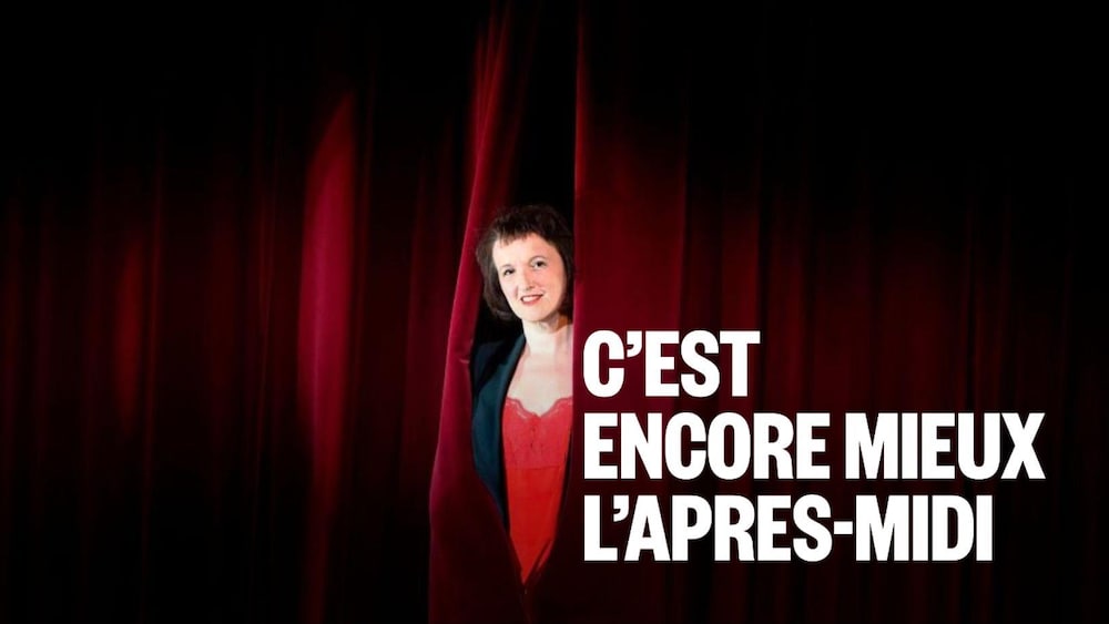 Photo d'Anne Roumanoff sur scène lors d'une session photo et se cachant à moitié derrière le rideau de scène.