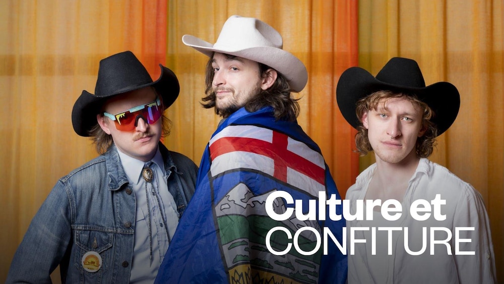 Trois hommes portant des chapeaux de cowboy, l'homme au centre à les épaules recouvertes d'un drapeau albertain.