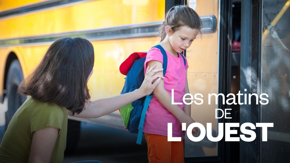 Une mère qui console sa jeune fille avant qu'elle monte à bord d'un autobus scolaire.