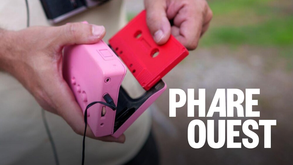 Un homme avec une caméra argentique rétro, portant un casque audio, insère une cassette audio rouge dans un lecteur portable rose.
