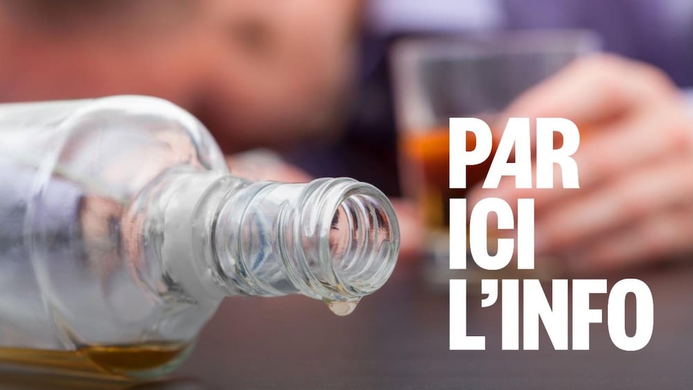Une personne tient un verre d'alcool et une bouteille vide sur une table.