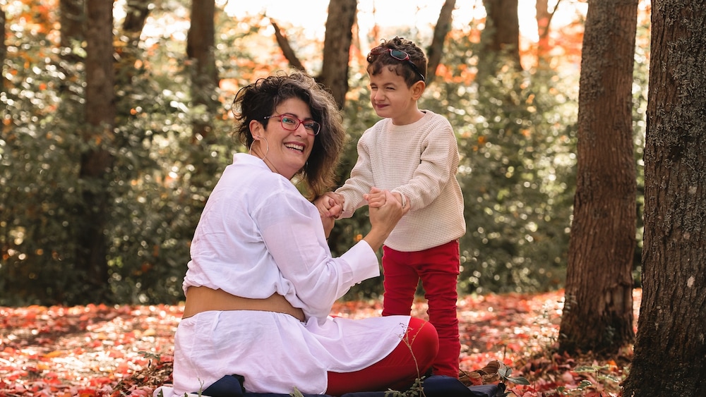 Dounia Daoud assise sur le sol dans une forêt. Elle tient les mains de son fils, Amir.