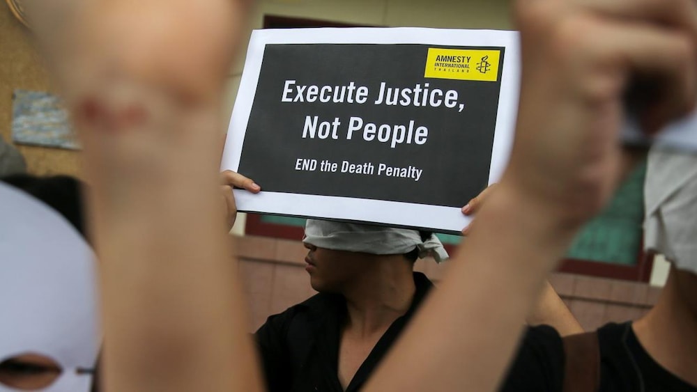 Une dame tient une pancarte qui dit « Execute Justice, Not People».