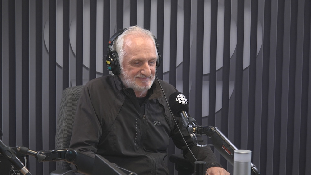 ortrait de l'artiste et sculpteur acadien André Lapointe assis dans un studio de radio, portant un casque d'écoute devant un micro.