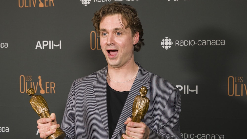 Un homme tient deux statuettes.