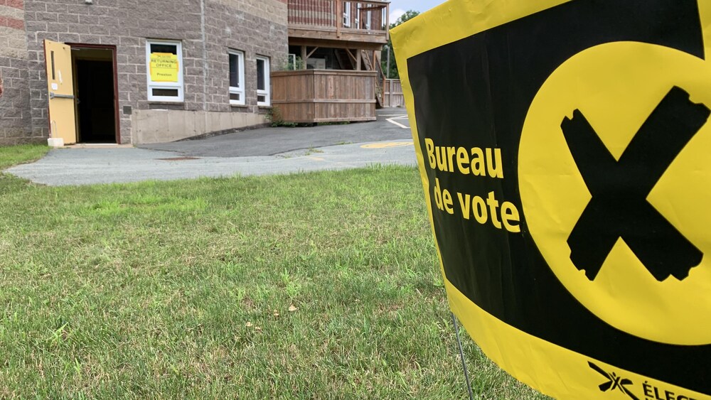 Plantée dans le gazon près d'un immeuble à la porte ouverte, une affiche jaune et noire d'Élections Nouvelle-Écosse avec les mots « Bureau de vote » en français.
