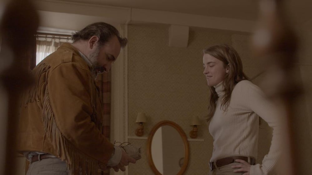 Un homme est devant une femme dans une chambre. Ils regardent ce qu'il tient dans sa main, soit un paquet enveloppé .