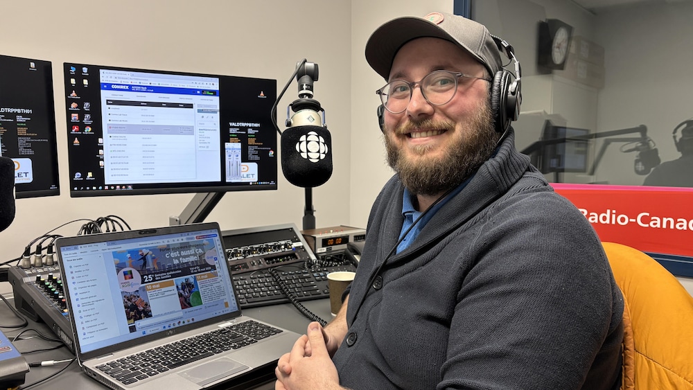 Erwann Boulanger, assis dans un studio de Radio-Canada, sourit à la caméra.