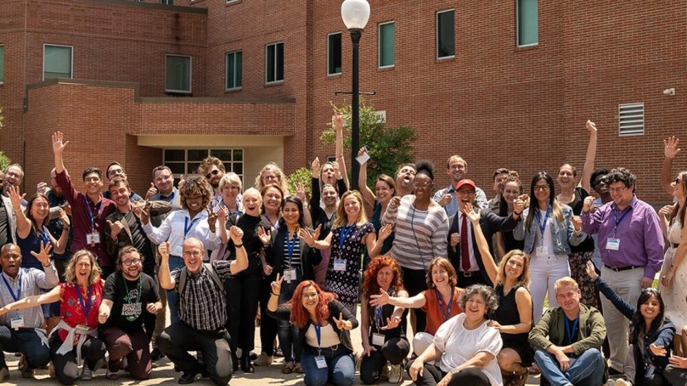 Une photo de groupe des participants, tout sourire et les bras levés, devant un pavillon en briques de l'Université du Québec à Montréal.
