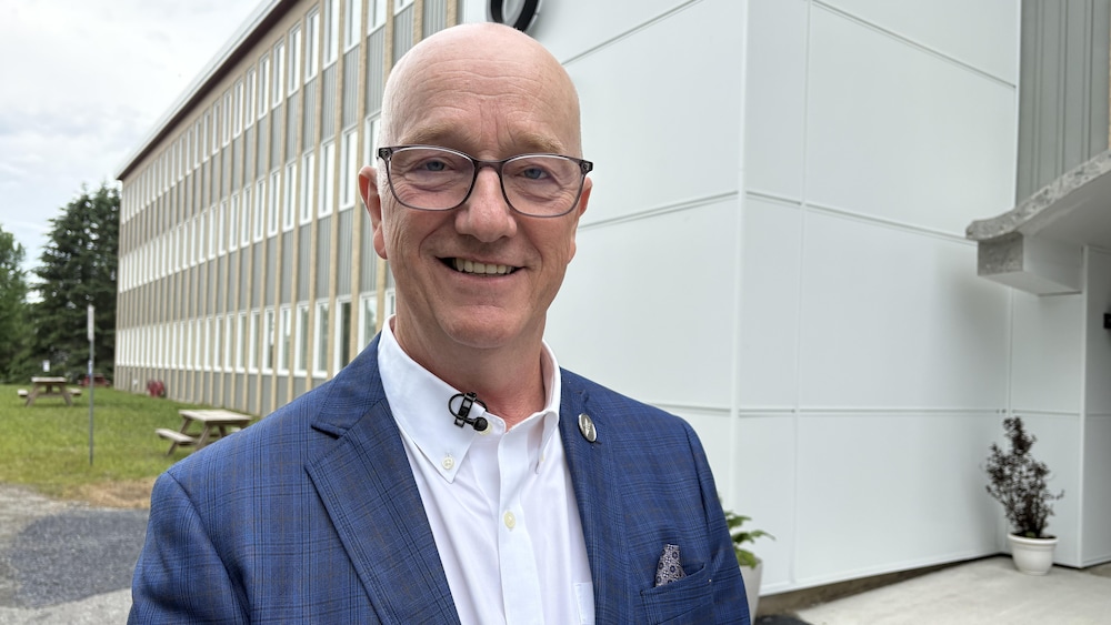 Debout à l'extérieur devant un bâtiment, Gérald Arseneault sourit en regardant vers la caméra.
