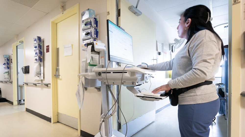 Une femme de profil travaillant sur un ordinateur dans un corridor de l'hôpital Jean-Talon