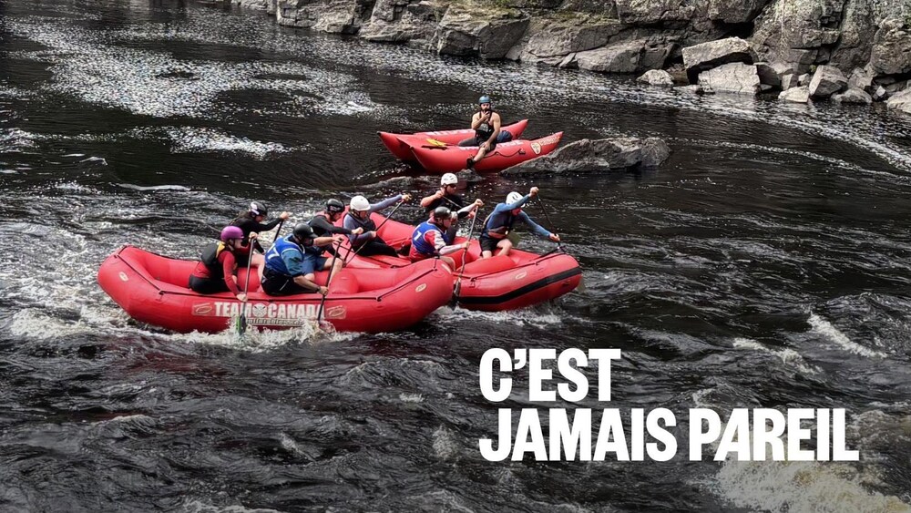 Plusieurs radeaux pneumatiques rouges et un kayak jaune naviguent sur une rivière sombre menant à des rapides. Le cours d'eau est encastré dans une gorge aux parois rocheuses et escarpées, surmontées d'une forêt de conifères.