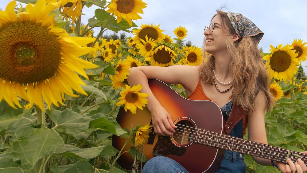 Une jeune musicienne tient une guitare dans un champ de tournesol.