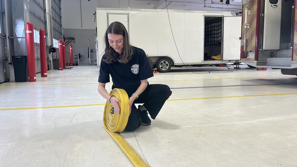Makayla Gaudet enroule un boyau d'arrosage dans la caserne des pompiers.