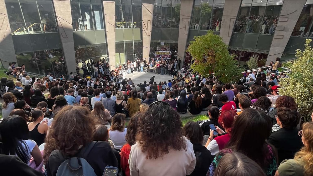 Foule d'étudiants vue de dos rassemblée dans une cour intérieure bordée d'un bâtiment moderne aux façades colorées