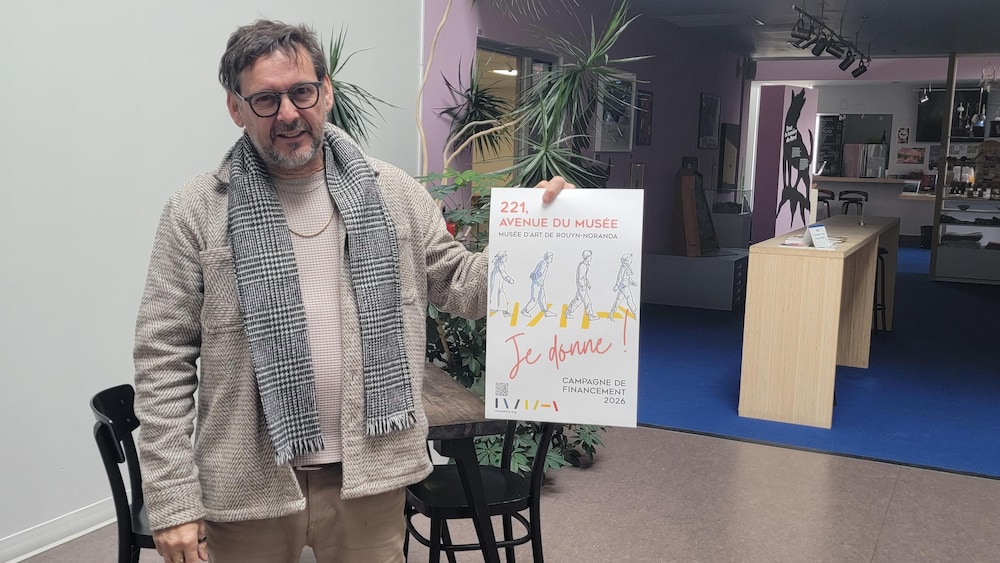 Jean-Jacques Lachapelle pose dans le musée avec une affiche faisant la promotion de la campagne de financement 2026.
