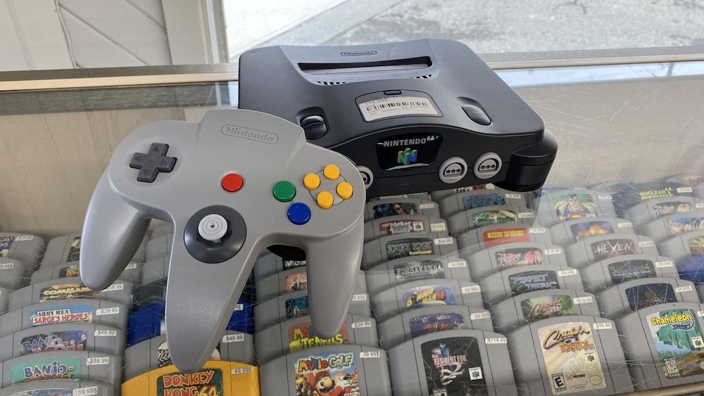 Une console Nintendo 64 posée sur une vitrine. Dans la vitrine, des dizaines de cassettes de jeux.