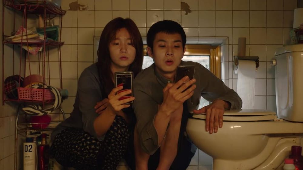 YouTube / MadMan Films Un adolescent et une adolescente regardent leur cellulaire en étant accroupis à côté d'une toilette.