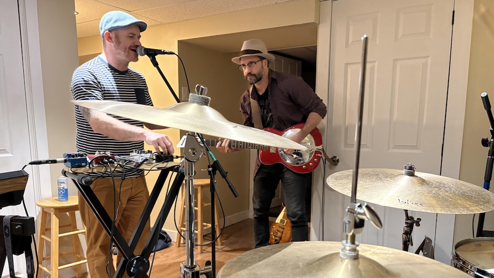 Frédéric Roy-Hall chante et Patrice Barbe le regarde en jouant de la guitare.