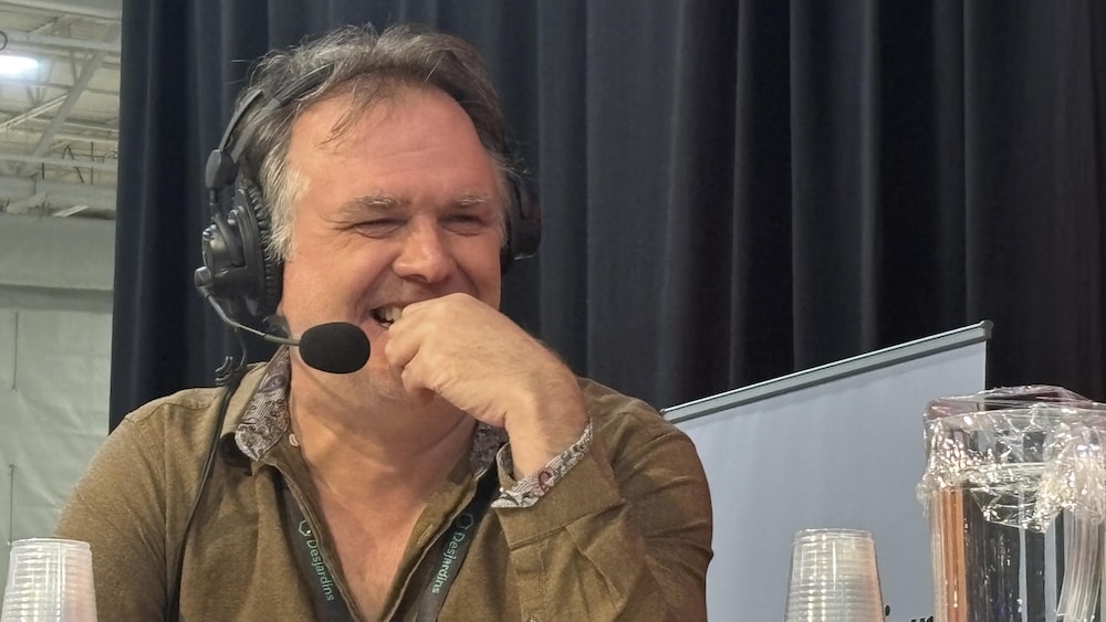 L'auteur est souriant, une main devant le visage, avec un casque d'écoute.