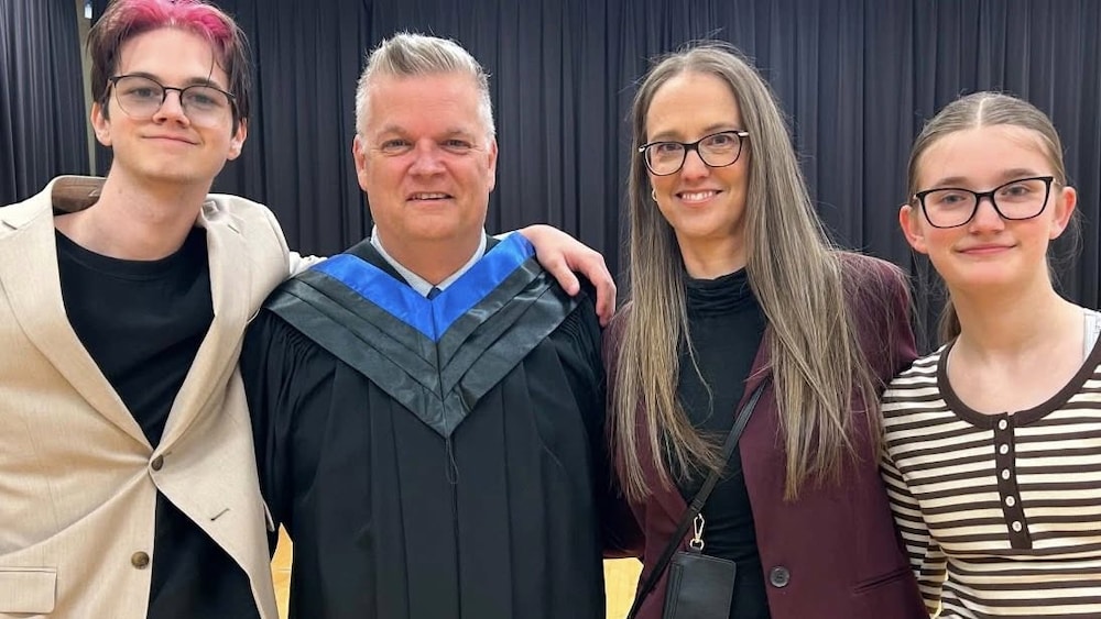 Un homme en toge de diplômé pose tout sourire aux côtés de sa famille.