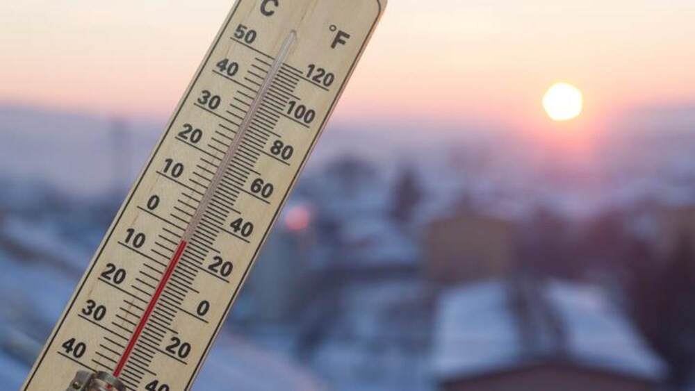 Un thermomètre se trouve devant un paysage ensoleillé.