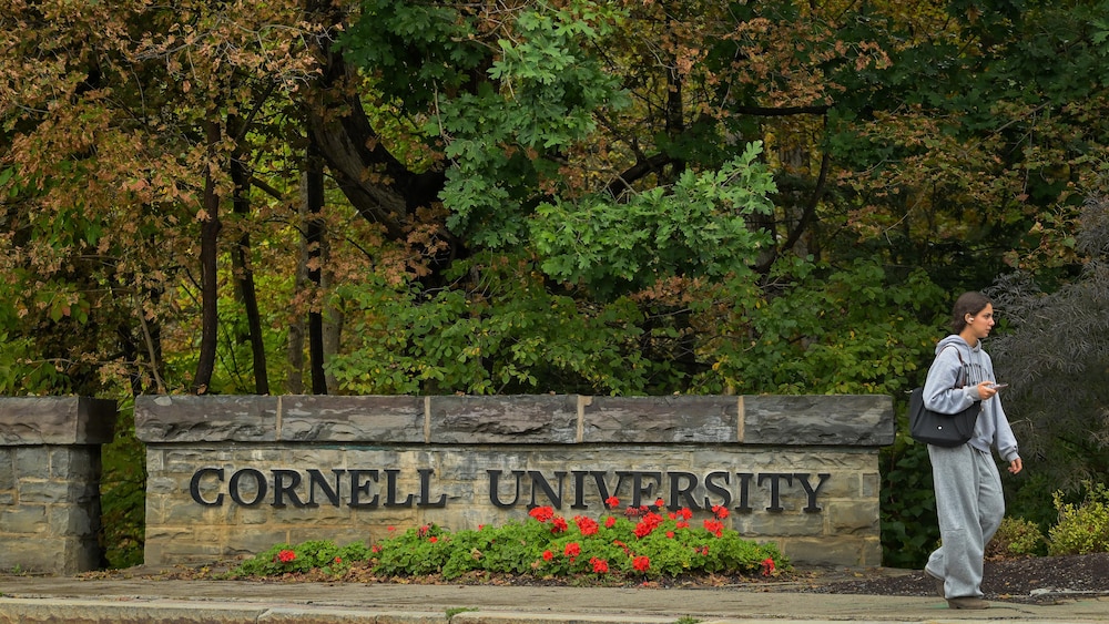 Une jeune femme marche devant l'enseigne de l'Université Cornell.