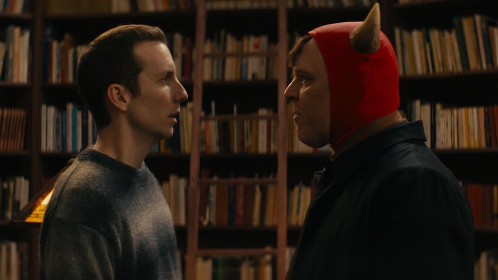 Entract Films Deux hommes, dont l'un est déguisé en démon, se font face devant une bibliothèque remplie de livres.