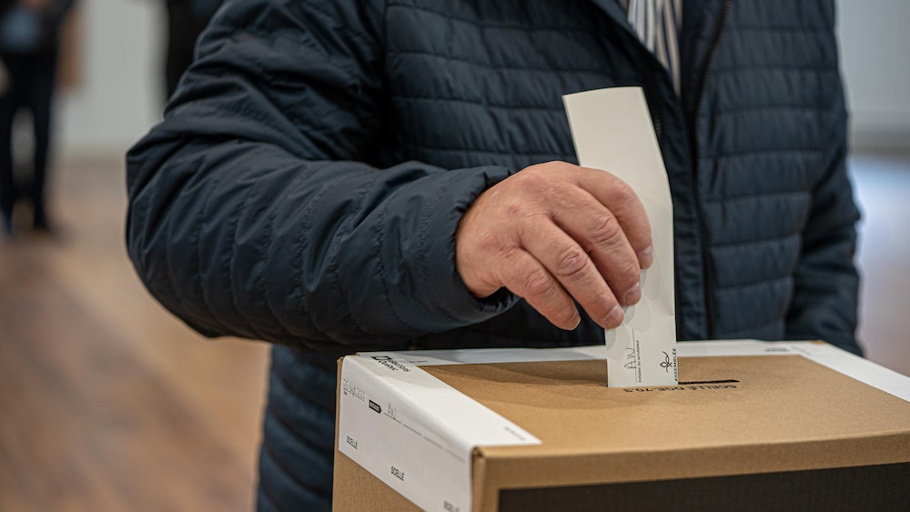 Un homme en train de déposer son bulletin de vote dans une boîte de scrutin.
