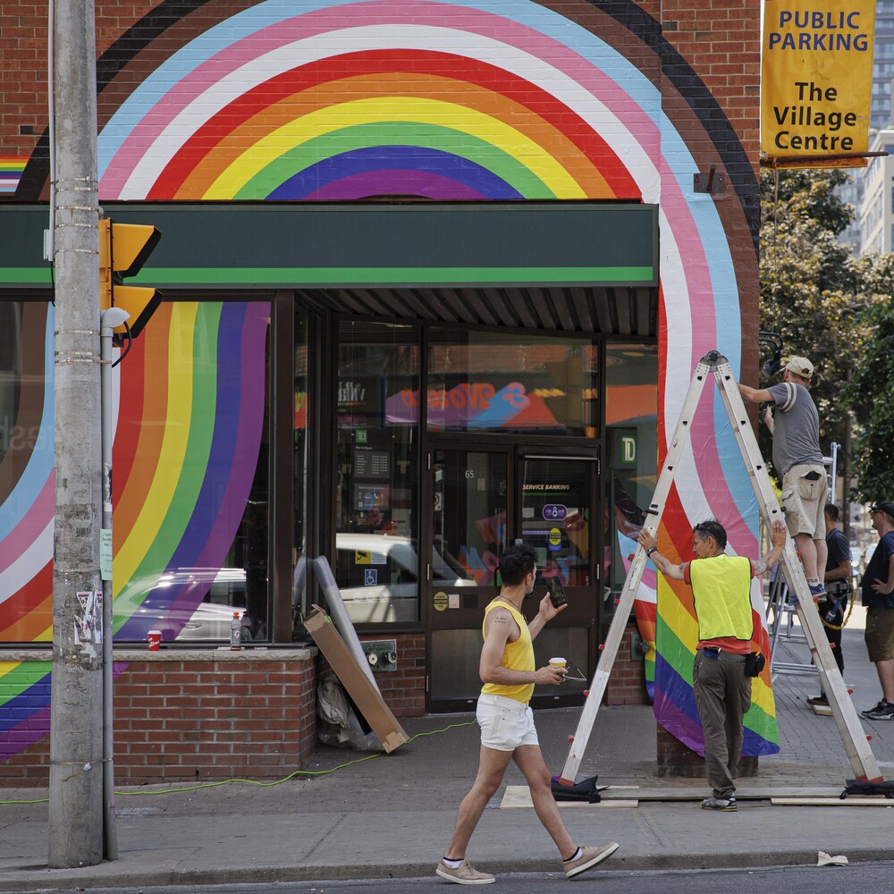 Des travailleurs installent une bannière arc-en-ciel à l'occasion du Mois de la Fierté dans le village gai de Toronto, sur la rue Church.