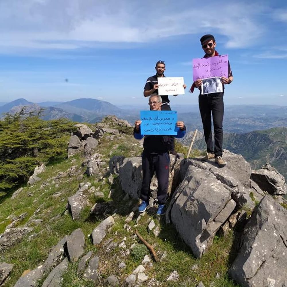 Trois Algériens brandissent des pancartes au sommet d’une montagne en Algérie.
