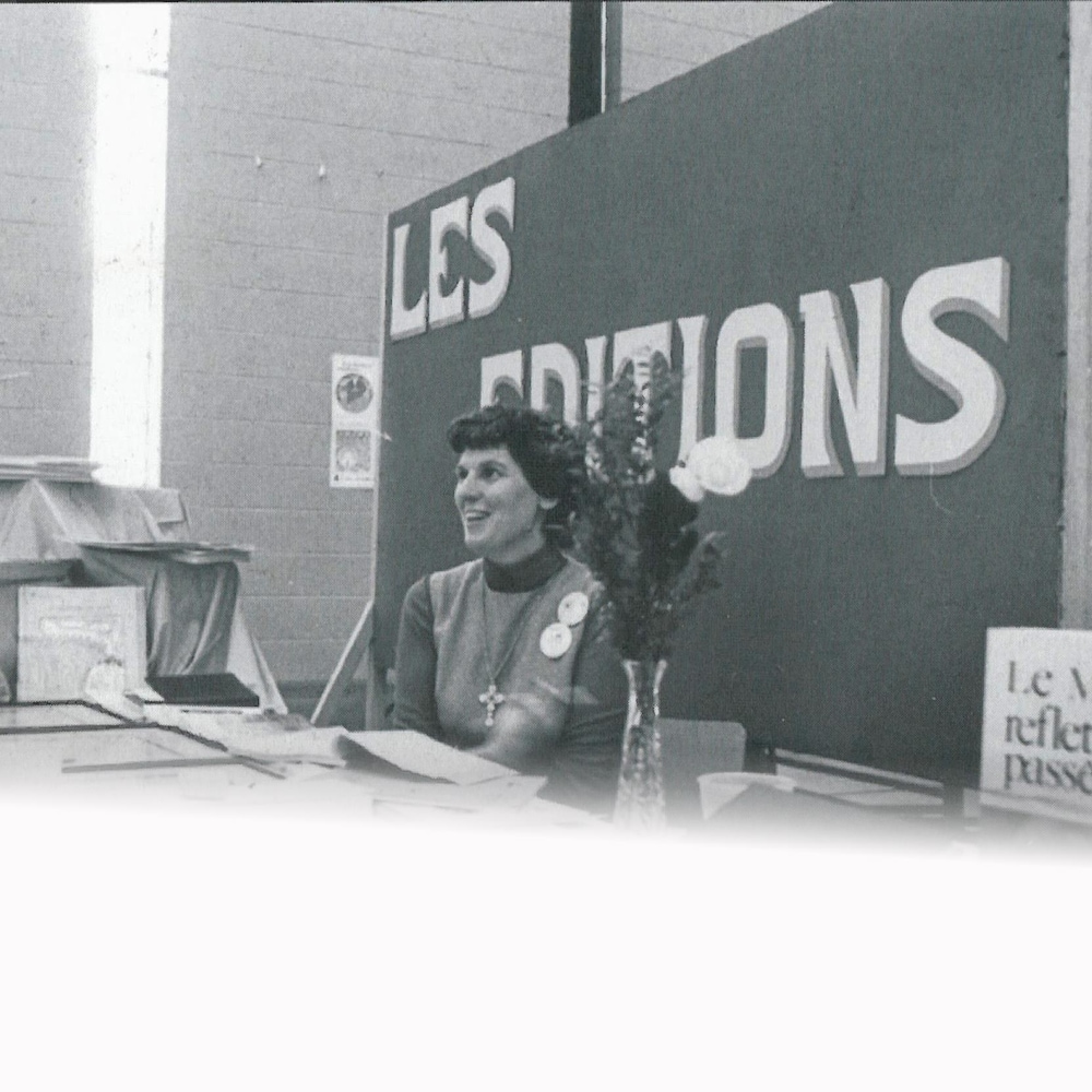 Photo d'Annette Saint-Pierre, en noir et blanc assise à son kiosque du Centre culturel franco-manitobain. 