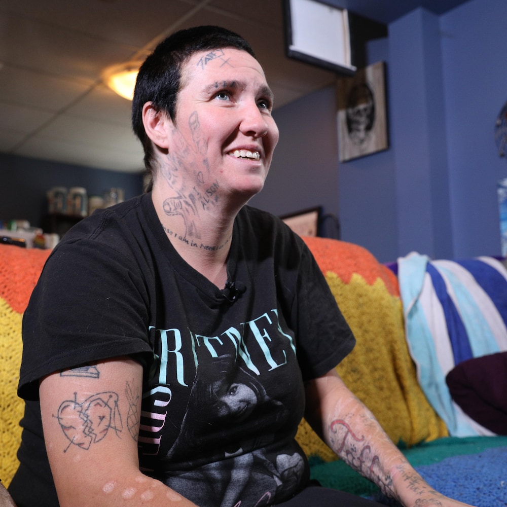 Une femme, Becks Dudley, avec beaucoup de tatouages, est assise sur un divan