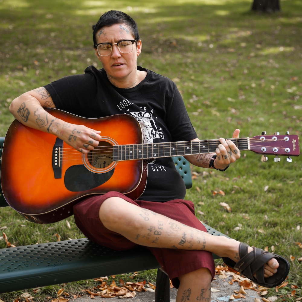 Becks Ducley qui joue de la guitare assise sur un banc de parc