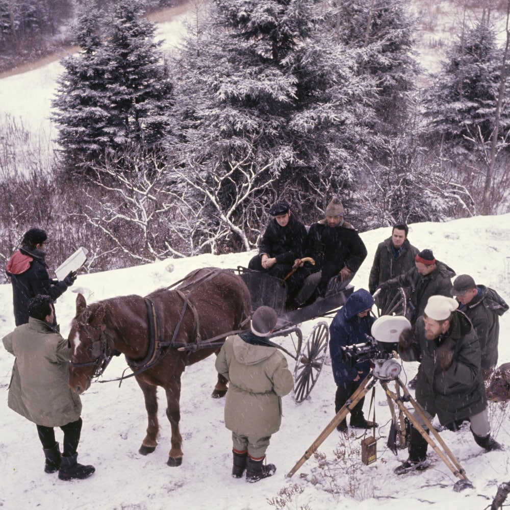 Équipe de tournage techniciens, caméraman, réalisateur et deux hommes dans une calèche, neige au sol.