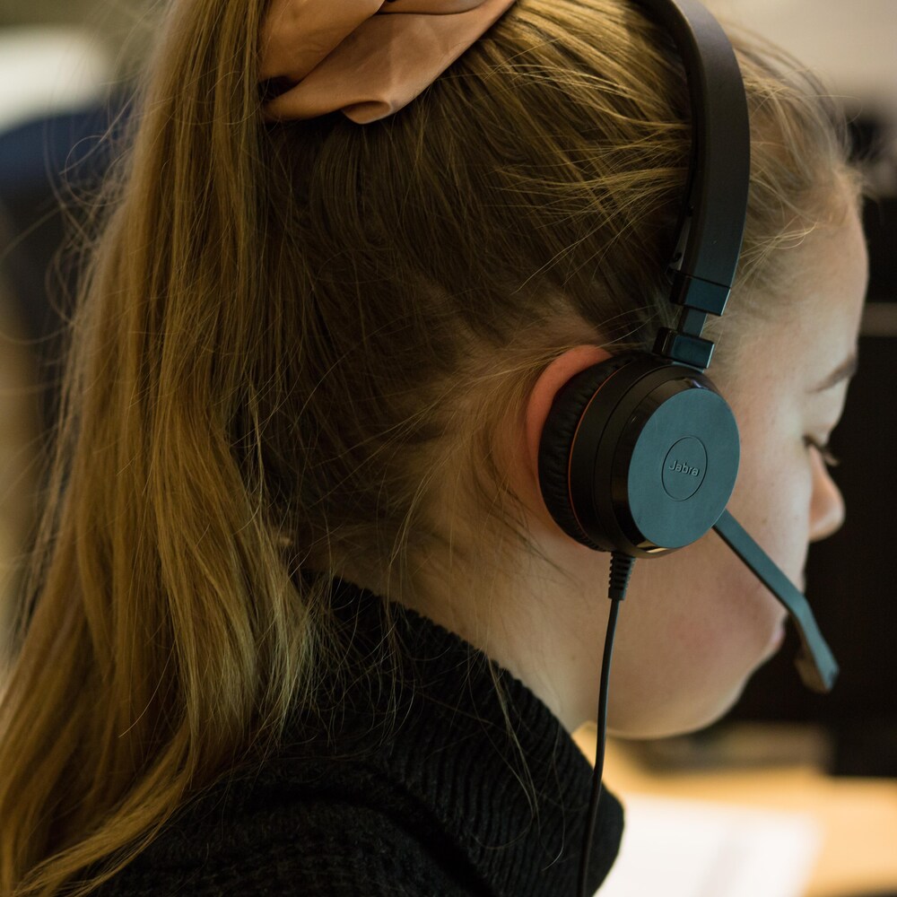 Une jeune femme avec un casque d'écoute regarde son écran.