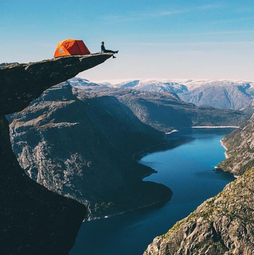 Une personne est assise au bout d'un pic rocheux sur lequel elle a installé leur tente à Trolltunga en Norvège.