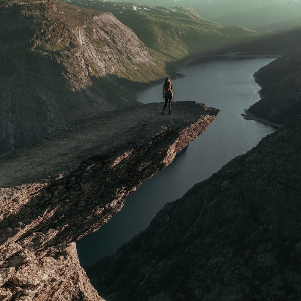 Une jeune femme se fait prendre en photo sur un pic rocheux au-dessus d'une falaise à Trolltunga en Norvège.