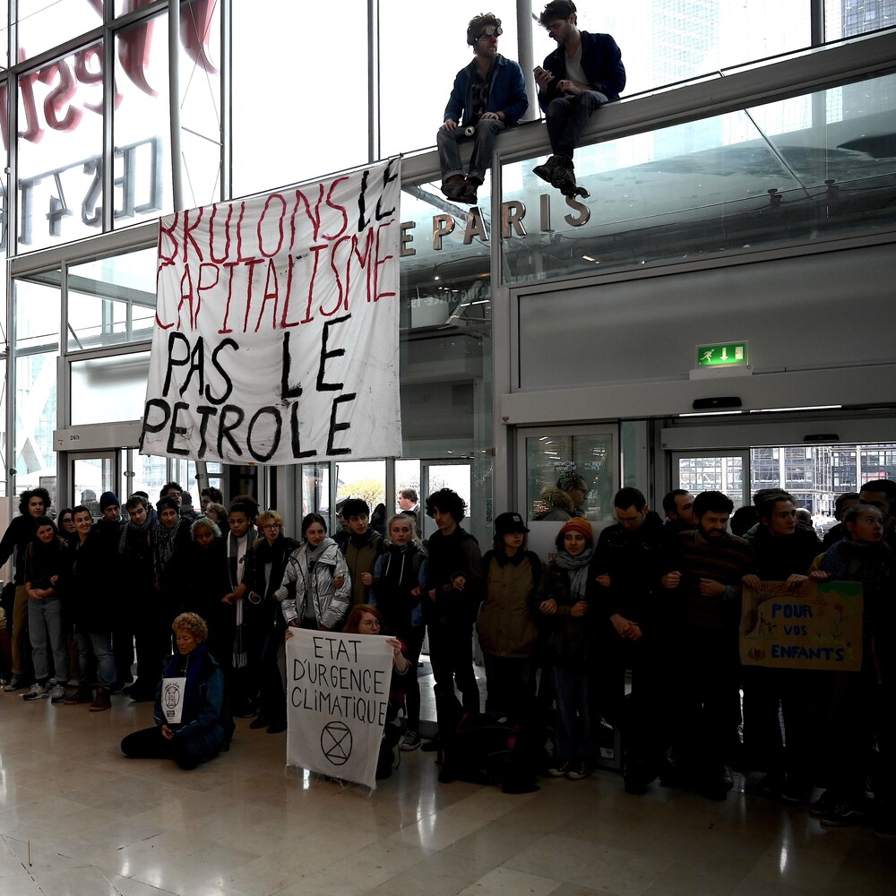 Des dizaines de jeunes se tiennent par le bras sous une banderole où l'on peut lire : « Brûlons le capitalisme, pas le pétrole ».