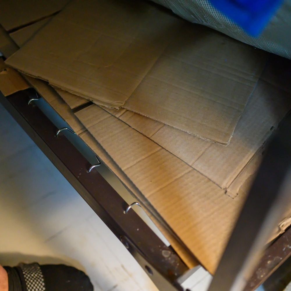 Un prisonnier de 84 ans soulève son mince matelas sous lequel il a placé des morceaux de boîtes de carton pour le rendre plus confortable. Il préfère dormir dans son fauteuil roulant.