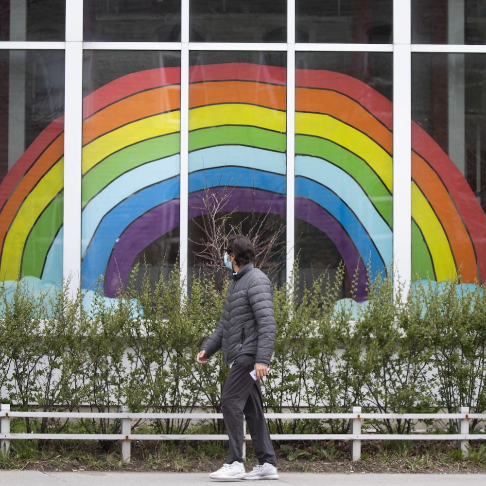 Un homme passe devant une fenêtre où est affiché un énorme dessin d'arc-en-ciel.
