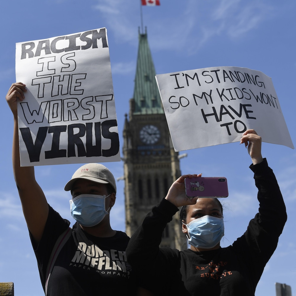 Deux personnes tiennent des pancartes devant le parlement à Ottawa.