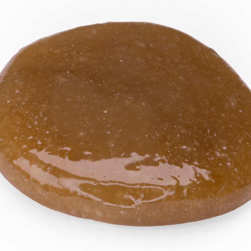 Image d'une substance visqueuse de couleur brunâtre sur fond blanc.