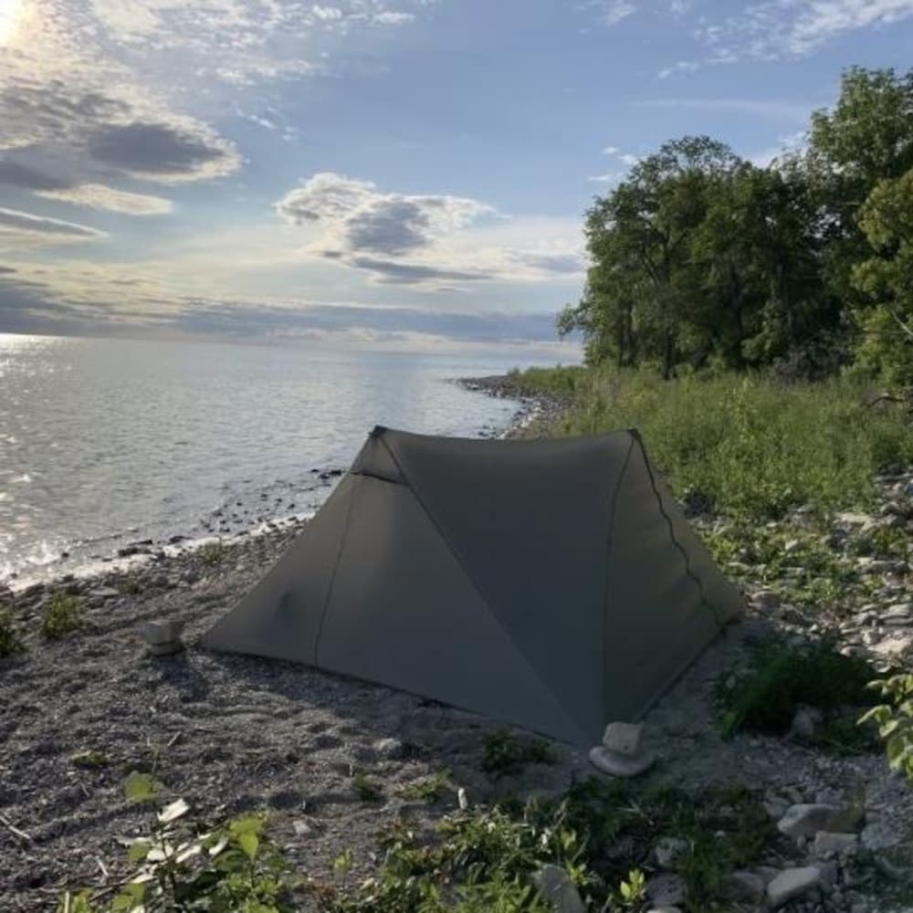 Une tente grise installée sur la plage d'un lac.