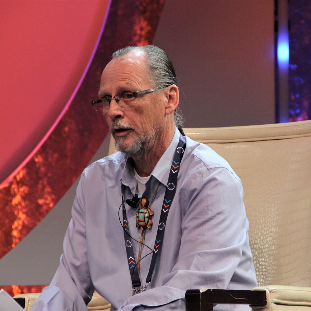 John Martin assis sur un fauteuil lors d'un panel de discussion.