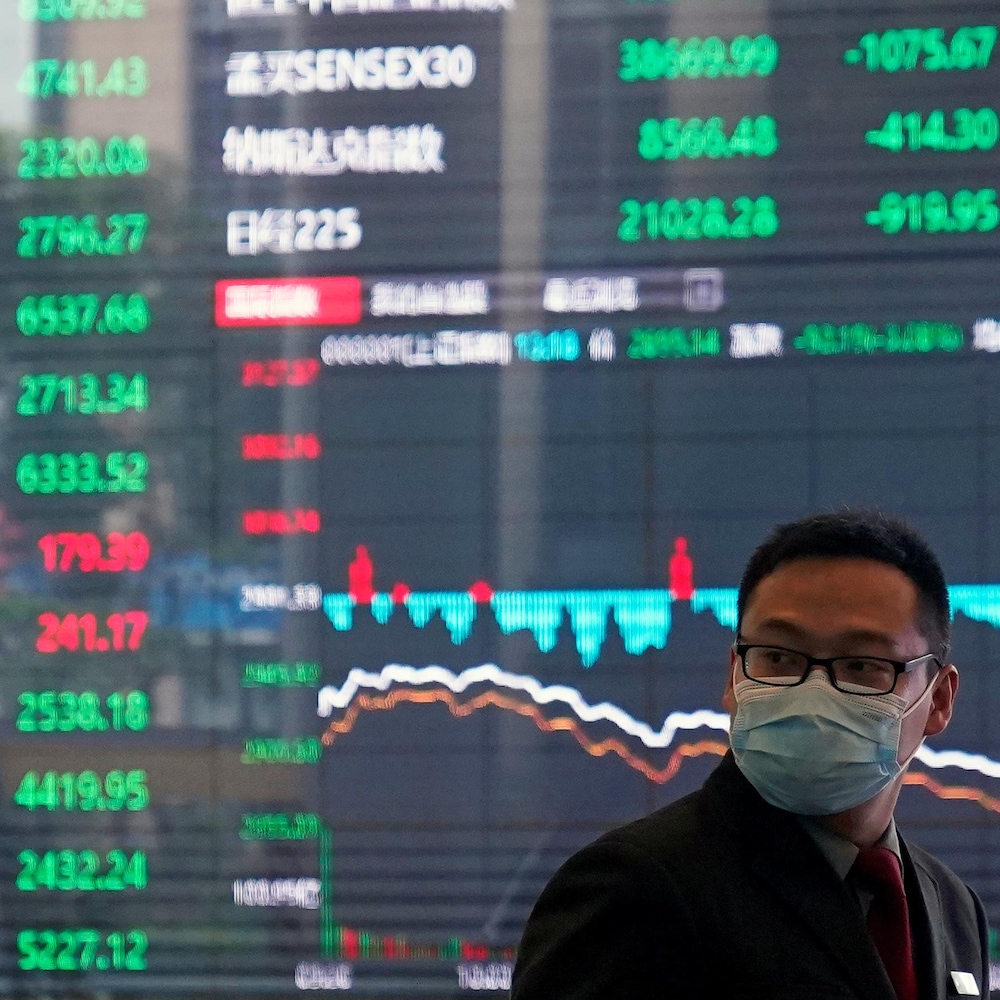 Un homme avec masque protecteur à la Bourse de Shanghai, dans le district financier de Pudong. En toile de fond, un immense tableau numérique présentant l'évolution des cours boursiers.