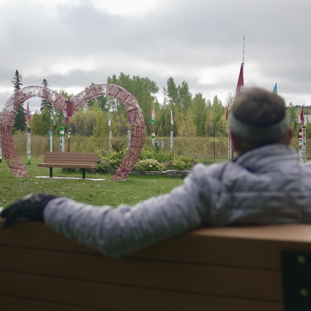 Un homme assis sur un banc fixe une structure en forme de cœur.