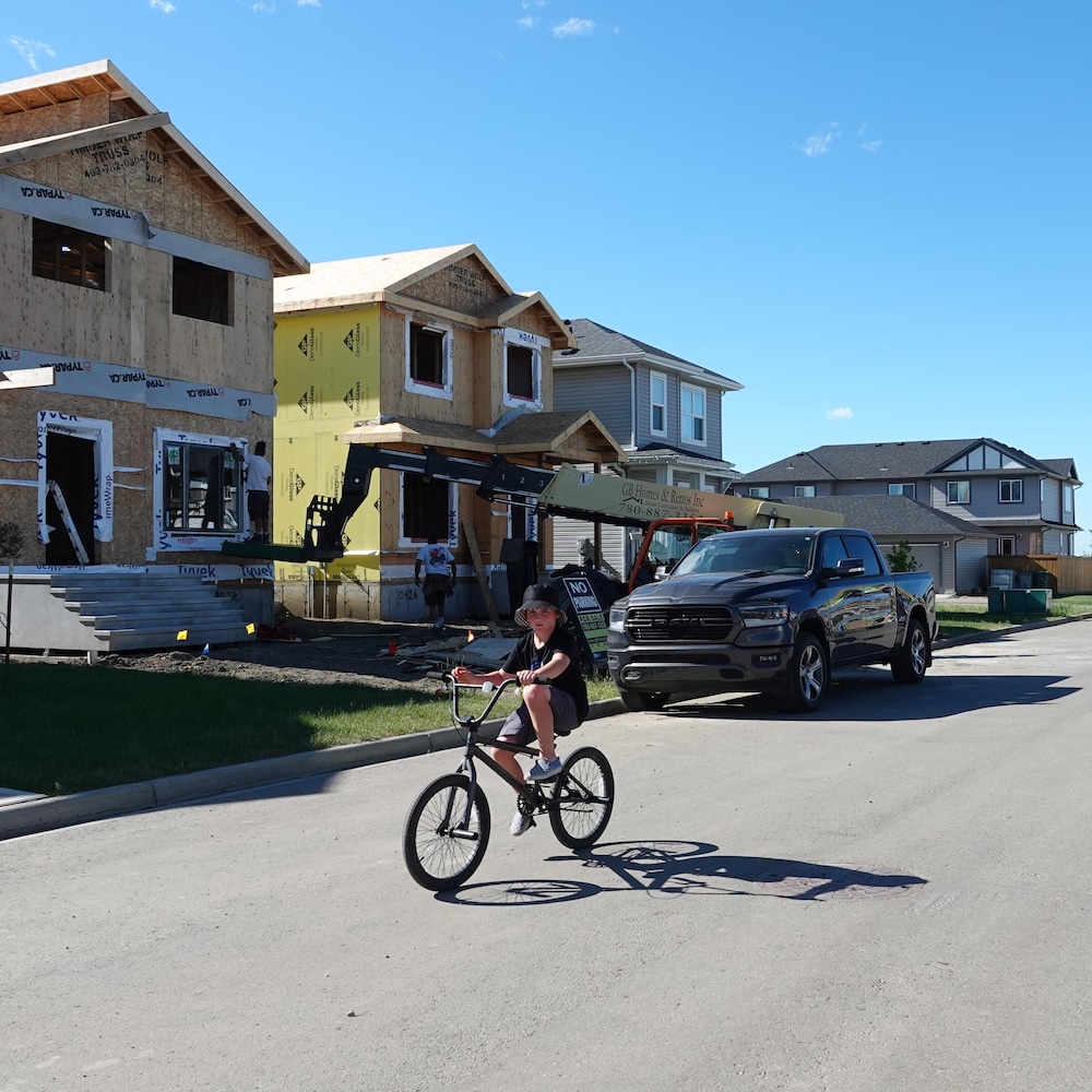 Un enfant à bicyclette dans une rue bordée de maisons en construction.