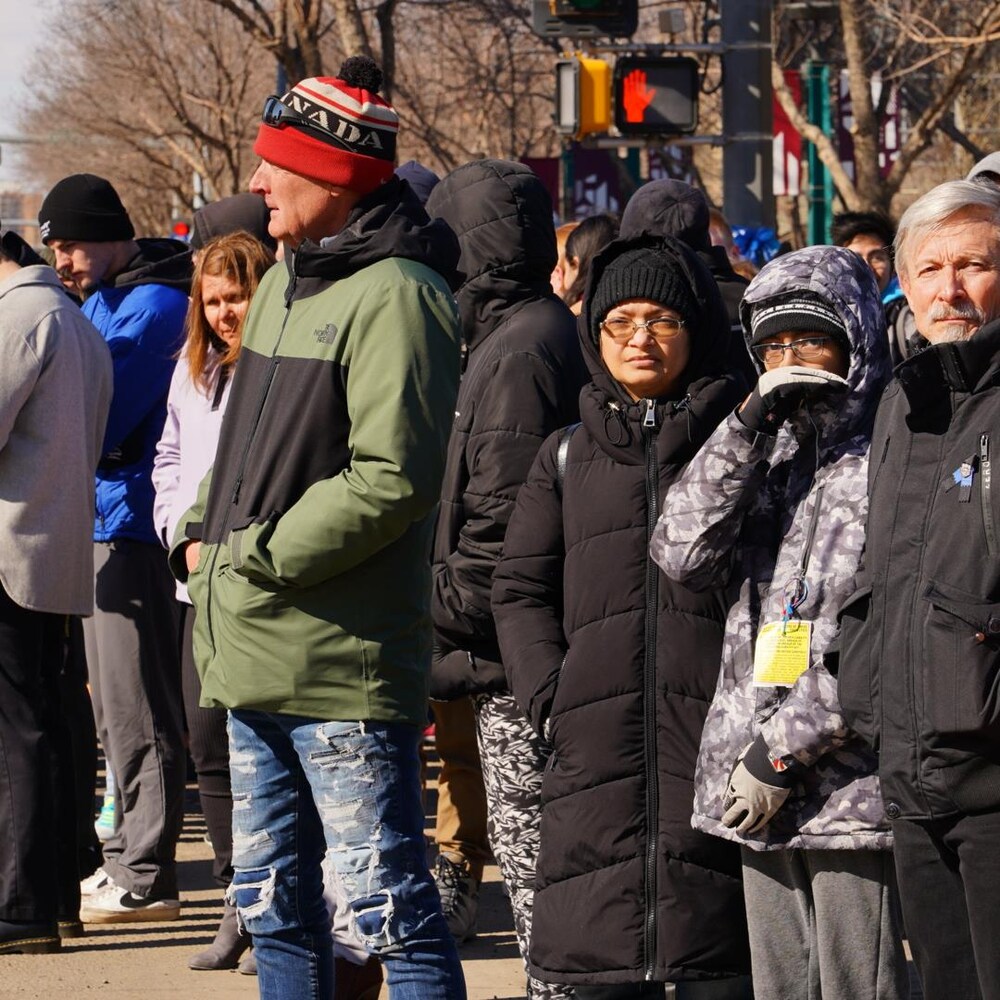 Plusieurs personnes sont sur le côté de la rue pour observer le cortège.