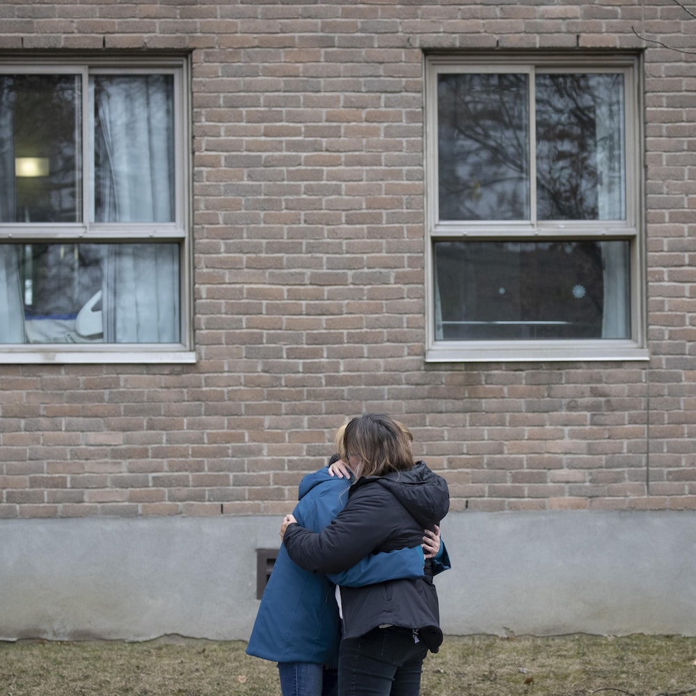 Un couple enlacé devant un mur fenestré.